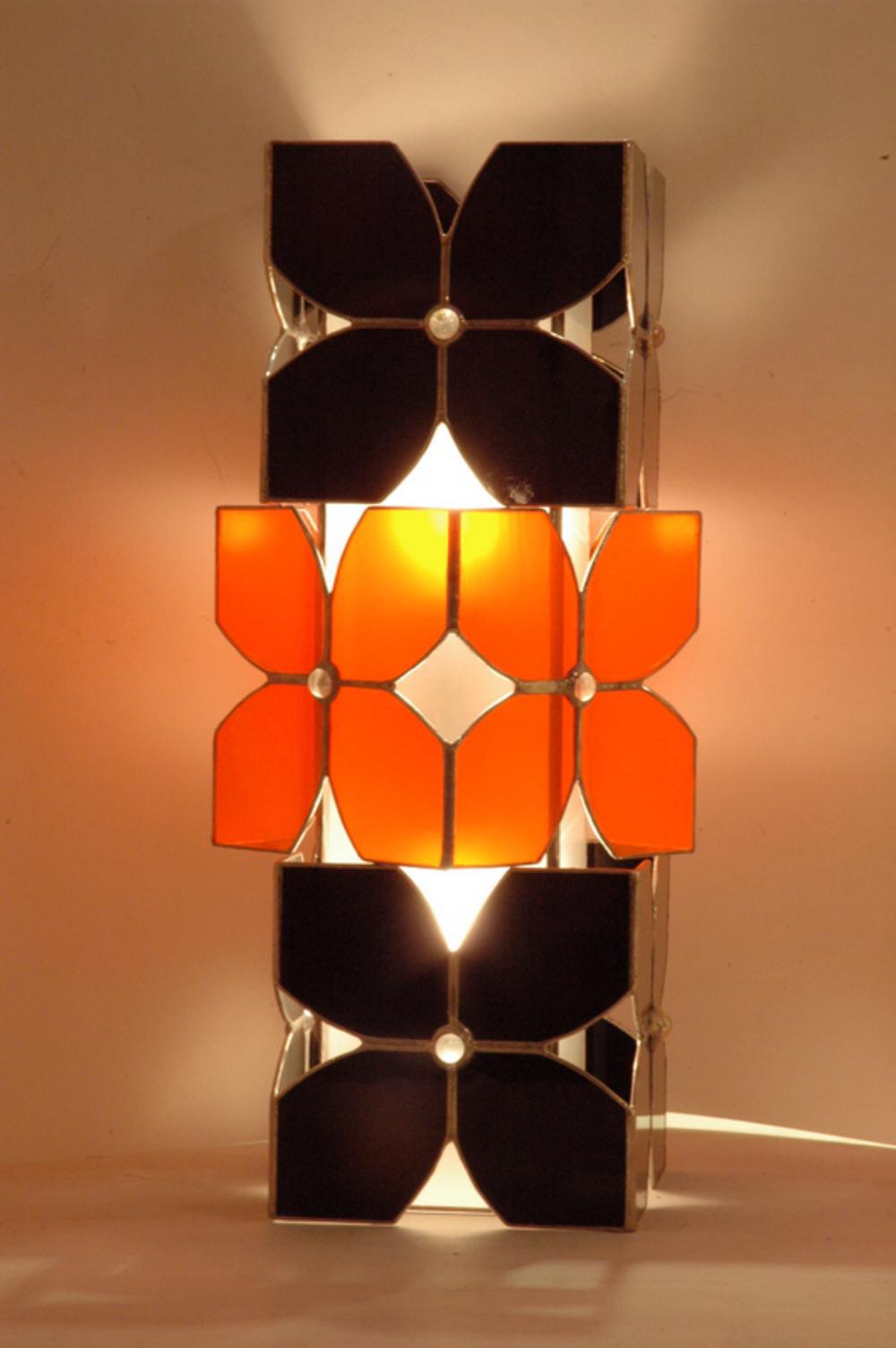 Vitraux oranges et noirs pour cette lampe à poser. Equipée de deux ampoules elle constitue une source de lumière intéressante en lampe d'appoint intégrée à la déco, sur un bureau ou une table de chevet.